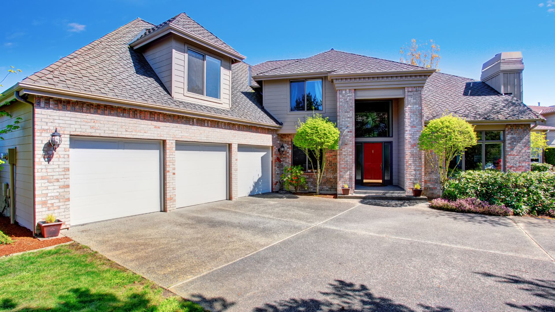 Large suburban house with three-car garage, red door, and manicured landscaping