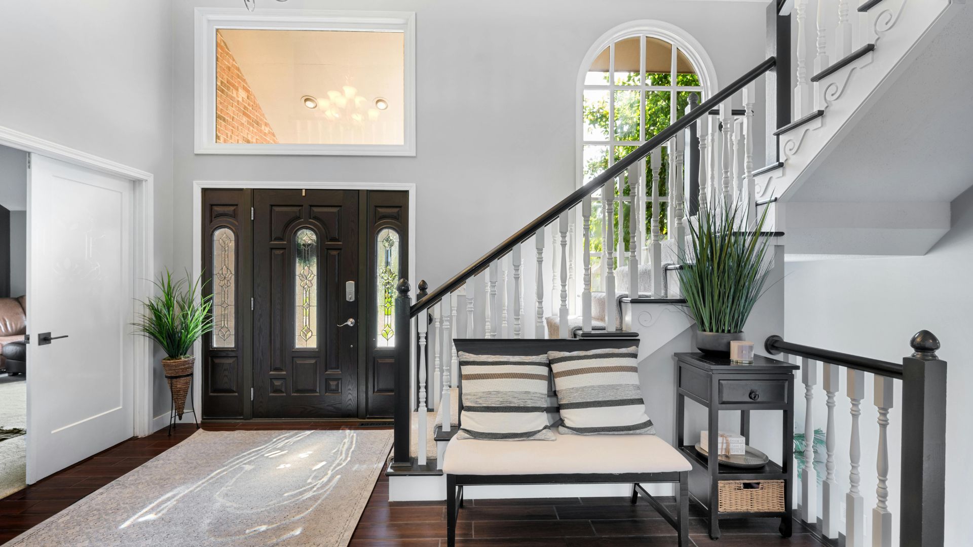 Elegant entryway with dark front door, white staircase, and decorative plants