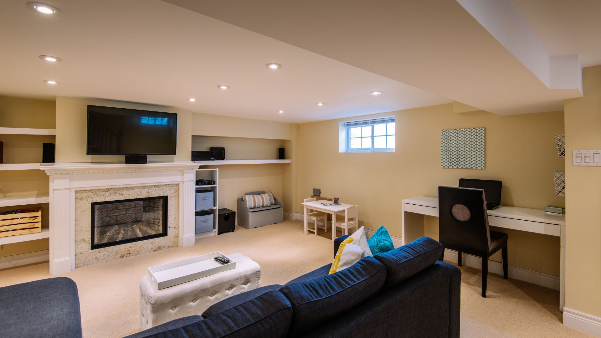 Cozy basement living room with fireplace, TV, blue couch, and work area