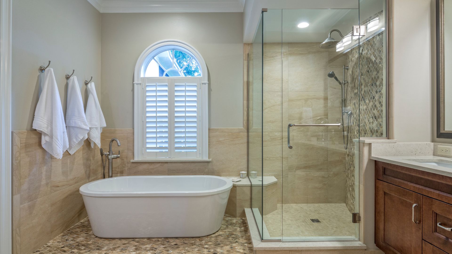 Luxurious bathroom with freestanding tub, glass shower, and arched window