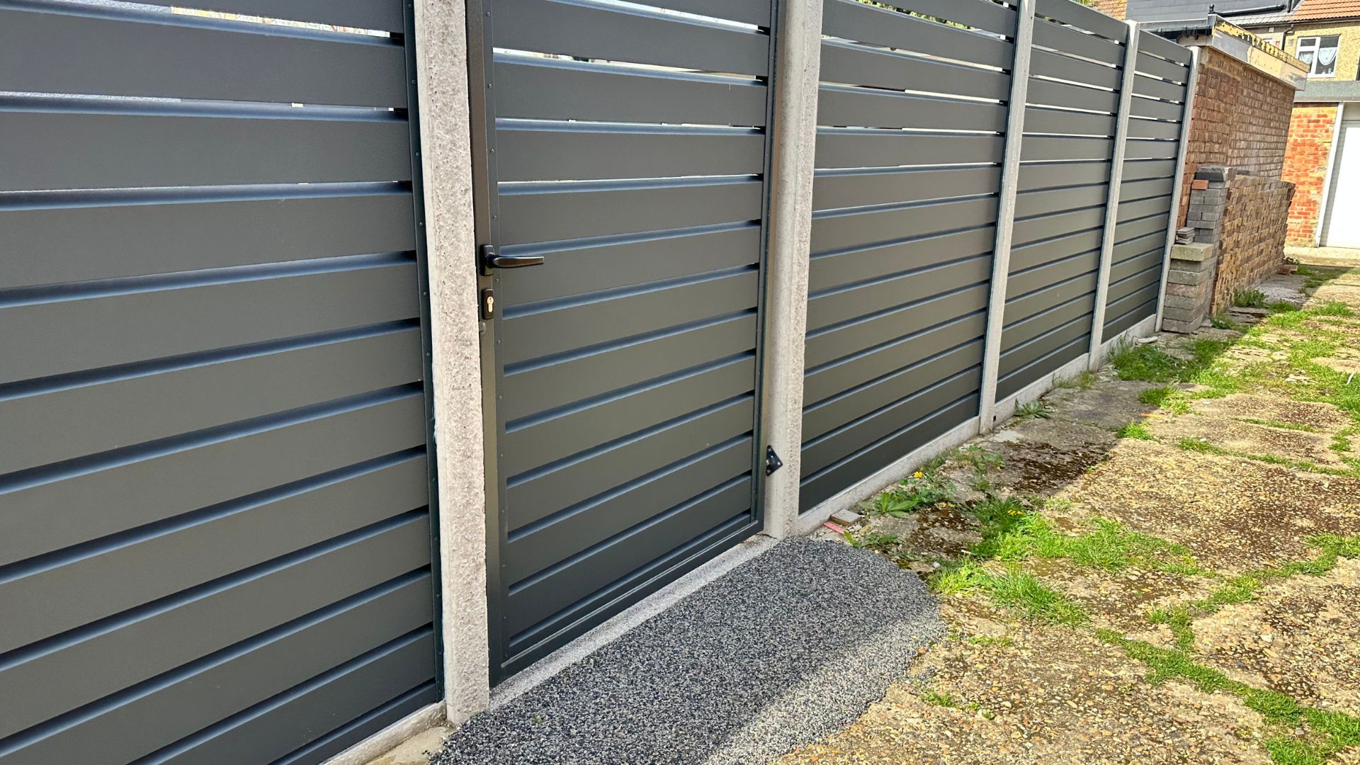 Modern gray metal fence with gate and concrete posts near brick wall