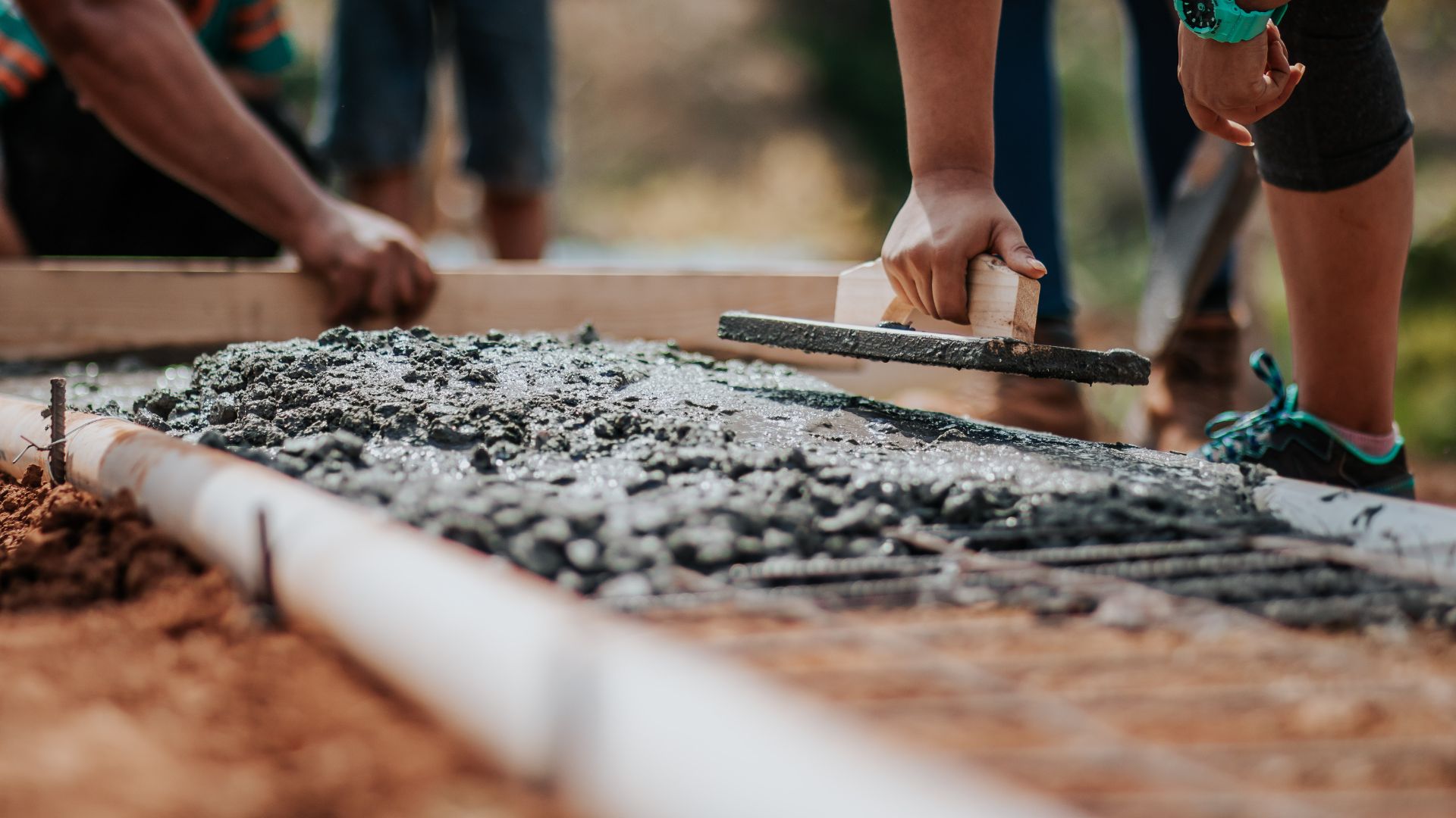 Workers leveling wet concrete with tools during construction project