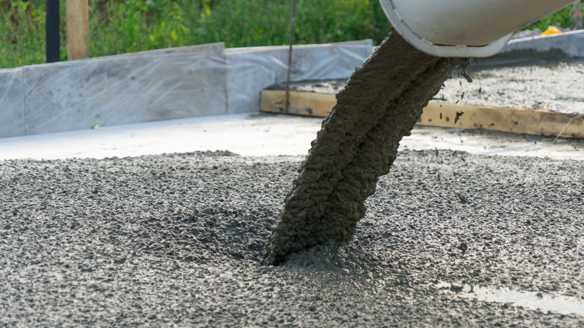Concrete pouring from mixer chute onto gravel foundation during construction