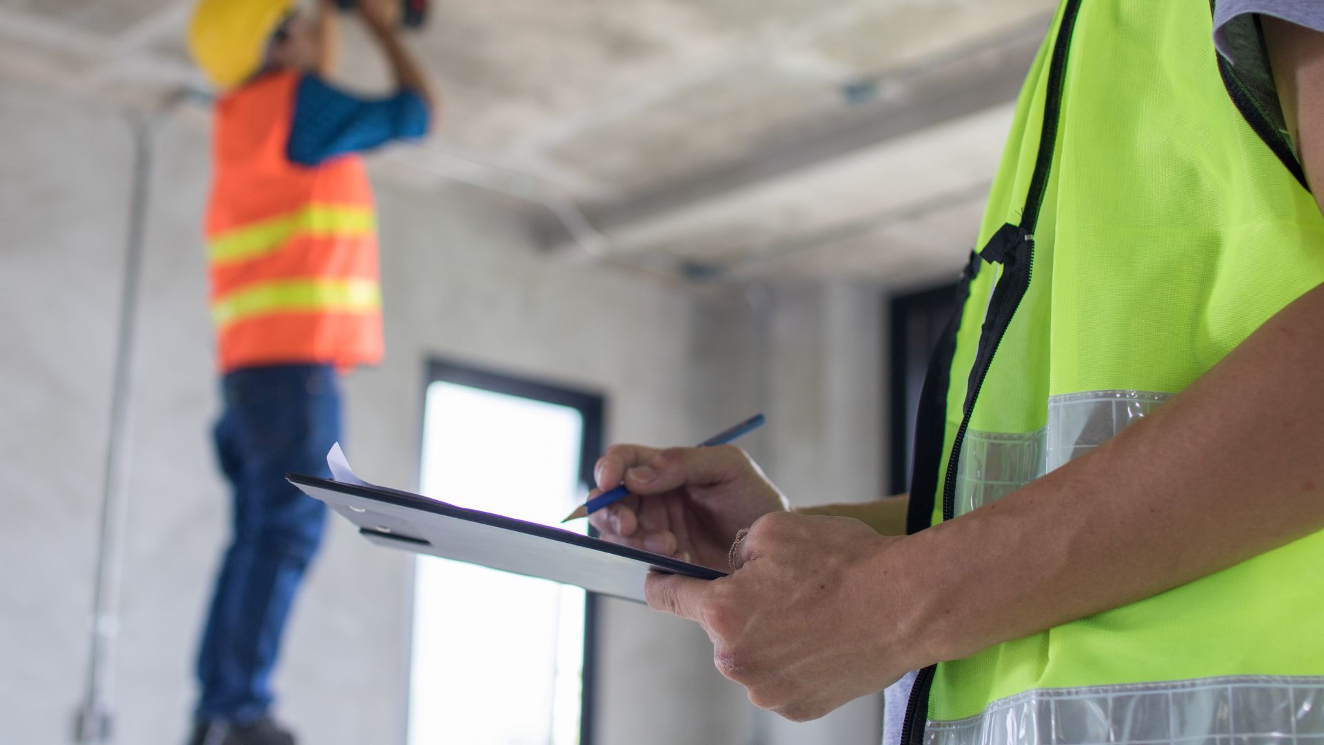Construction workers in safety vests reviewing documents on tablet at site